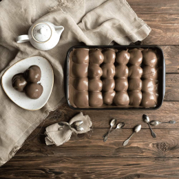 Profiteroles al cioccolato in vaschetta, con glassa scura e consistenza cremosa, serviti in un contesto raffinato con stoviglie coordinate. Venduto da Orobica Food.