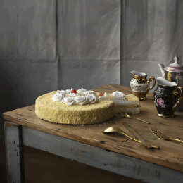 Torta mimosa decorata con panna montata e ciliegie, dalla superficie soffice e granulosa, presentata su tavolo in legno con servizio da tè elegante. Venduto da Orobica Food.