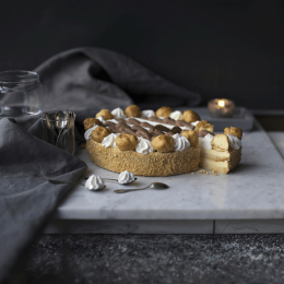 Torta Saint-Honoré con crema e bignè, decorata con panna e cacao, servita in ambientazione elegante con dettagli raffinati e luce soffusa. Venduto da Orobica Food.